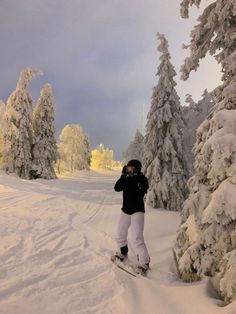 a person on skis standing in the snow next to some trees and snow covered ground