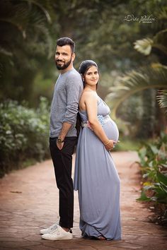 a pregnant couple standing next to each other on a path in the woods with palm trees