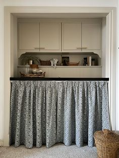 a kitchen with white cupboards and black counter top covered by a gray ruffled table skirt