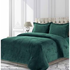 a bed with green comforter and pillows in a white room next to a lamp