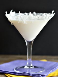 a drink in a martini glass with coconut garnish on the rim and yellow napkins