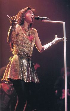 a woman in a gold dress holding a microphone and singing into a mic on stage