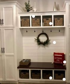 an entryway with white cabinets and baskets on the wall, wreaths hanging above