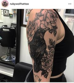 a woman's arm with a black bird and flowers on it, sitting in front of a mirror