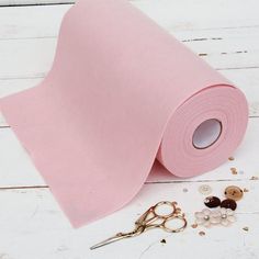 a roll of pink paper next to scissors and buttons on a white wooden surface with other crafting supplies