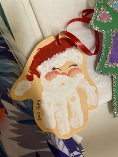 a handprinted santa clause ornament next to a christmas tree ornament