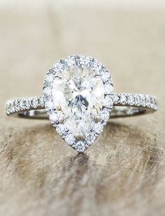 a pear shaped diamond ring on top of a wooden surface with diamonds around it and the band