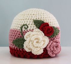 a crocheted hat with flowers on it sitting on top of a white table