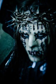 a woman with black makeup and nails on her face, wearing a crown of spikes