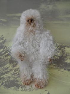 a fluffy white stuffed animal sitting on top of a green and gray background with mountains in the distance