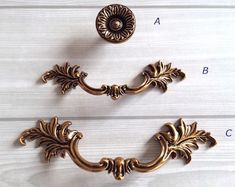 two ornate brass pulls on a white painted wood surface, one has an acantic design