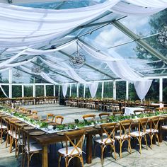 an outdoor dining area with tables, chairs and white drapes on the ceiling is decorated with greenery