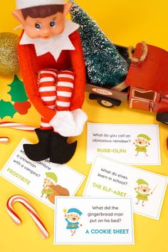 an elf sitting on top of a table next to some candy canes and cards