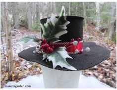 a black hat with holly leaves and red berries on the brim is sitting in front of some trees