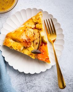 a white plate topped with a slice of pizza next to a fork and bowl of soup