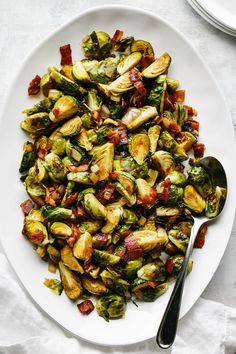 a white plate topped with brussel sprouts and bacon next to a fork