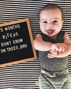 a baby standing next to a sign that says 5 months biceps don't grow on trees, bro