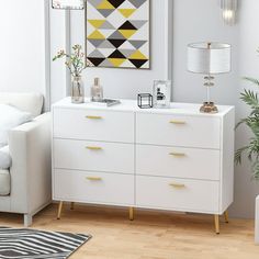 a living room with white furniture and a large painting on the wall above the dresser