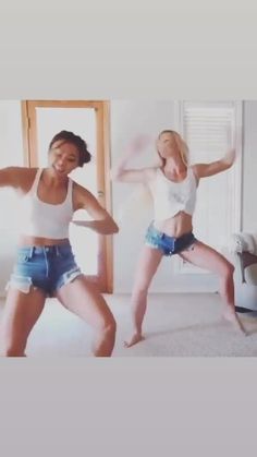 two young women are dancing in the living room with their legs spread out and one is wearing blue denim shorts