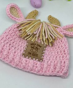 a crocheted pink hat with an egg in the middle and a brown tag on it