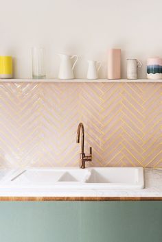 a white sink sitting under a faucet next to a wall mounted shelf filled with cups