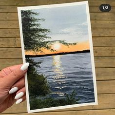 a person holding up a card with a sunset on the water and trees in the background