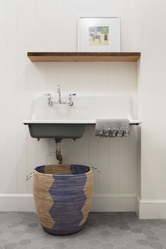 a bathroom sink sitting under a wooden shelf next to a white counter top with a blue and yellow basket underneath it