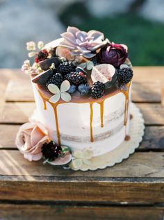 a white cake topped with berries and flowers on top of a wooden table covered in icing