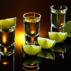 three shot glasses filled with limes on a black counter top next to slices of lime