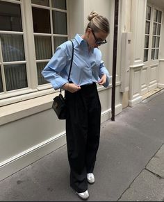 a woman standing on the sidewalk with her hands in her pockets and looking down at her purse