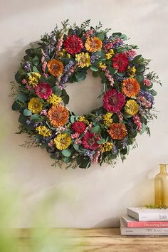 a wreath is hanging on the wall next to some books and vases with flowers