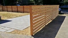 a wooden fence in the middle of a yard with grass on the ground and cars parked behind it