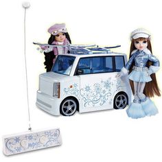 two dolls are standing next to a toy car with skis on the roof and snowboards on top