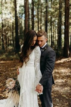 a bride and groom are standing in the woods with their arms around each other as they hold hands