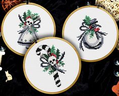 three cross - stitch christmas ornaments are shown on a black surface with other items around them