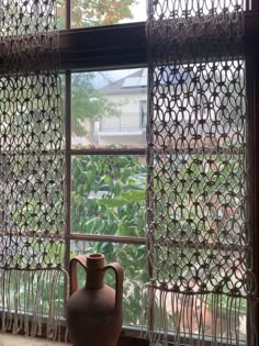 a vase sitting in front of a window with curtains on the outside and behind it