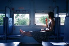 a woman sitting on a train seat looking out the window with her feet propped up