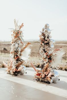 two christmas trees are decorated with flowers and silver baubs in the middle of an empty field