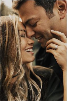 a man and woman smile as they hold each other close to their foreheads together