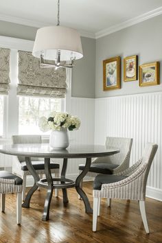 a dining room table with four chairs and a vase on top of it in front of a window