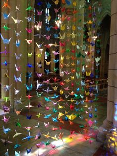 a room filled with lots of colorful paper cranes hanging from the ceiling and lights shining down on the floor