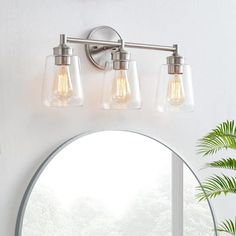 a bathroom vanity light with three lights on it and a round mirror in the corner