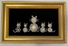 an ornate gold frame with pearls and brooches on black paper in front of a white wall