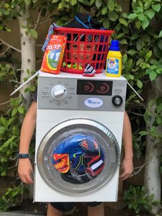 a young boy standing in front of a washing machine with laundry products on top of it