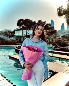 a woman holding a bouquet of flowers standing next to a pool