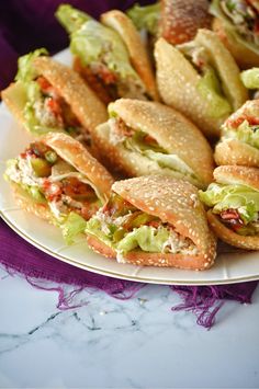 a white plate topped with sandwiches on top of a purple table cloth next to other food items