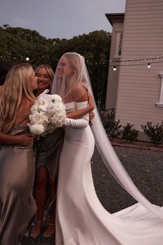 two bridesmaids hugging each other in front of a house with string lights on the side