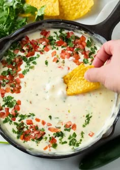 a person dipping tortilla chips into a skillet filled with quesadilla sauce