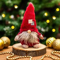 a red and white gnome figurine sitting on top of a wooden stump next to christmas decorations