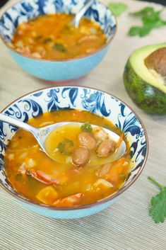 two bowls filled with soup next to an avocado on top of a table